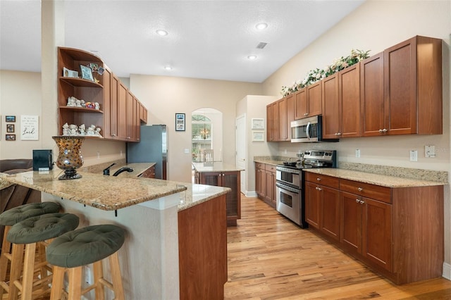 kitchen with appliances with stainless steel finishes, a kitchen breakfast bar, kitchen peninsula, light stone countertops, and light hardwood / wood-style floors