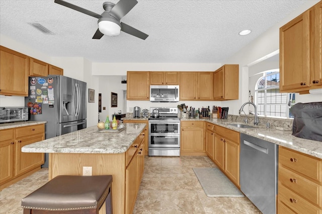 kitchen featuring sink, appliances with stainless steel finishes, a kitchen breakfast bar, a center island, and light stone counters