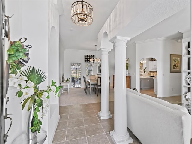 carpeted foyer featuring arched walkways, ornamental molding, tile patterned flooring, ornate columns, and a chandelier