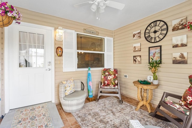 interior space with ceiling fan, wooden walls, and light tile patterned floors