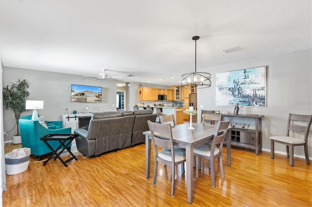 dining space with ceiling fan with notable chandelier, light hardwood / wood-style flooring, and a textured ceiling