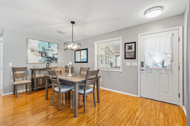 dining space with a notable chandelier, a textured ceiling, and light wood-type flooring