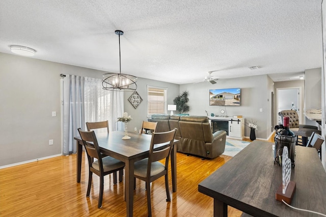 dining space featuring ceiling fan with notable chandelier, a textured ceiling, and light hardwood / wood-style floors