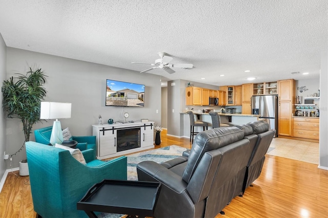 living room featuring ceiling fan, a textured ceiling, and light hardwood / wood-style flooring