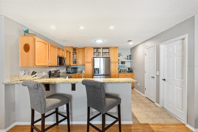 kitchen featuring light stone countertops, a breakfast bar area, stainless steel appliances, and kitchen peninsula