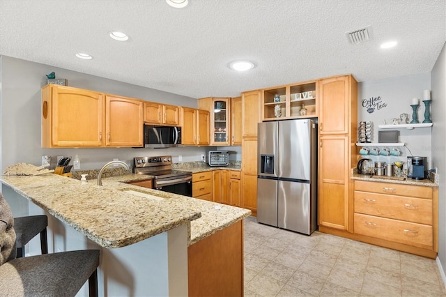 kitchen with sink, a breakfast bar area, stainless steel appliances, light stone counters, and kitchen peninsula