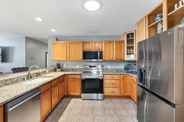 kitchen featuring sink, light stone countertops, kitchen peninsula, and appliances with stainless steel finishes