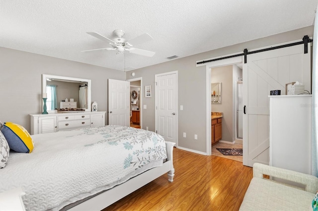 bedroom with connected bathroom, light hardwood / wood-style flooring, a textured ceiling, a closet, and a barn door