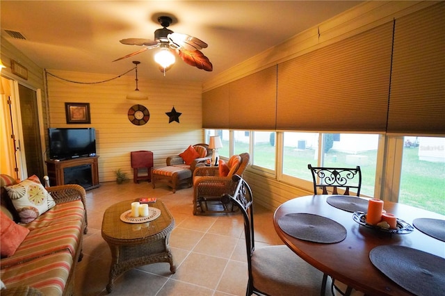 living room with ceiling fan, wooden walls, and light tile patterned floors