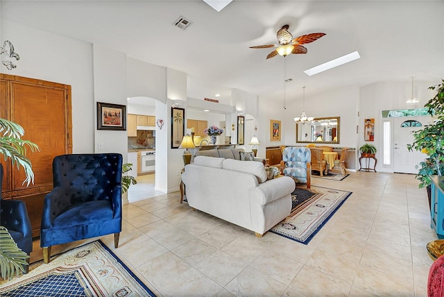 tiled living room featuring ceiling fan with notable chandelier, a skylight, and high vaulted ceiling