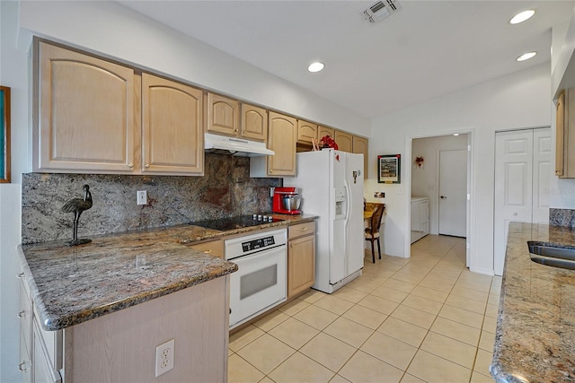 kitchen with white appliances, washer and clothes dryer, light brown cabinetry, vaulted ceiling, and dark stone counters