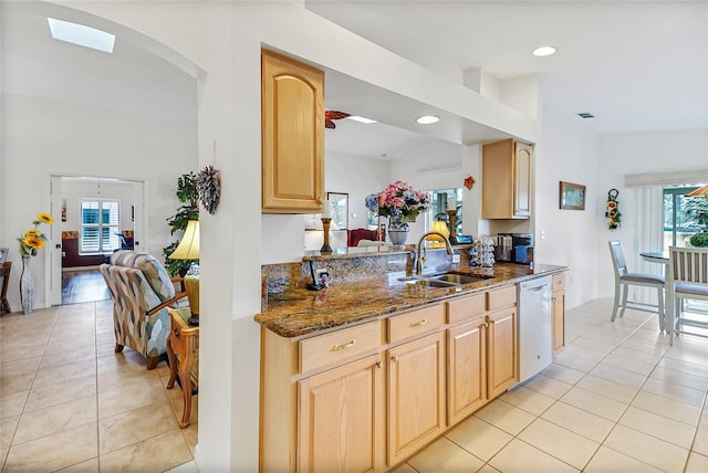 kitchen with dishwasher, sink, light brown cabinetry, and dark stone counters