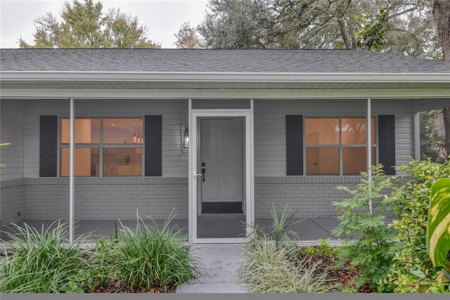 doorway to property with brick siding and a shingled roof