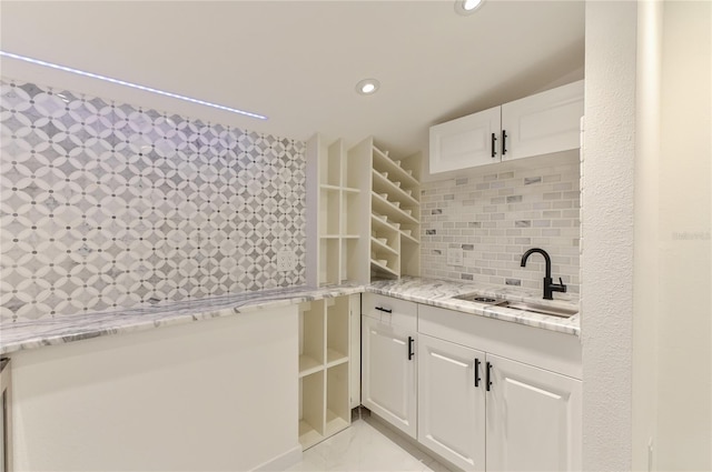 kitchen with tasteful backsplash, light stone countertops, recessed lighting, white cabinets, and a sink