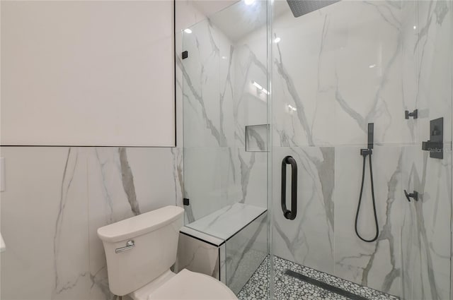 bathroom featuring a marble finish shower, toilet, and tile walls