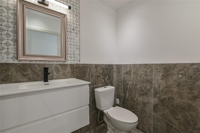 half bath featuring toilet, tile walls, wainscoting, and vanity