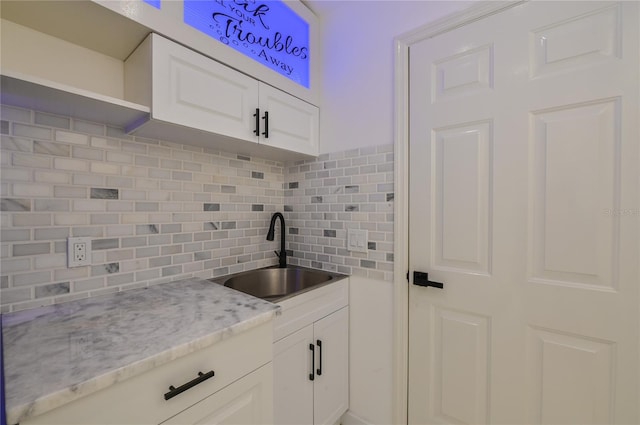 kitchen with a sink, light stone counters, tasteful backsplash, and white cabinets