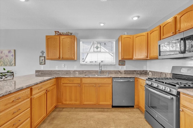 kitchen with light stone counters, appliances with stainless steel finishes, kitchen peninsula, and sink