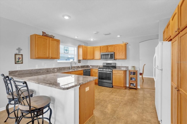 kitchen featuring a breakfast bar, sink, dark stone counters, kitchen peninsula, and stainless steel appliances