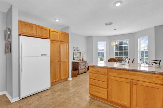 kitchen featuring decorative light fixtures, light stone countertops, and white fridge