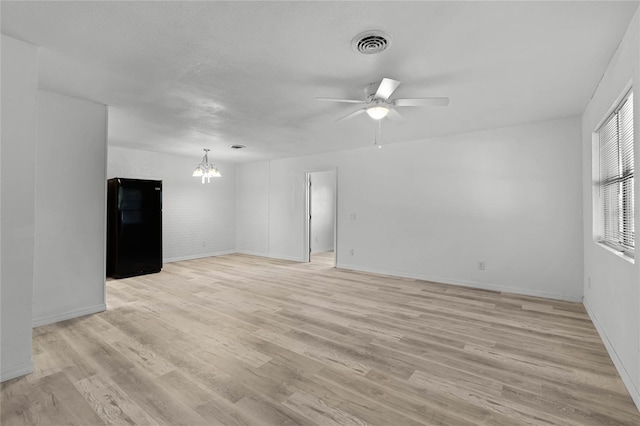 unfurnished room featuring ceiling fan with notable chandelier, light wood-type flooring, visible vents, and baseboards