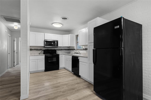 kitchen with light wood finished floors, light countertops, black appliances, white cabinetry, and a sink