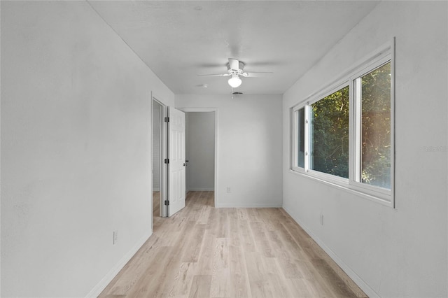 empty room with light wood-type flooring, a ceiling fan, and baseboards