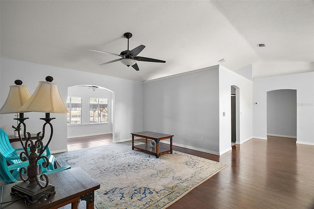 living area with arched walkways, ceiling fan, lofted ceiling, dark wood-type flooring, and baseboards