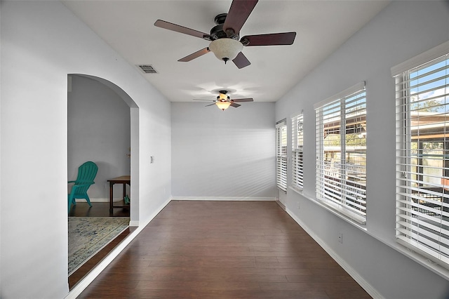 empty room featuring baseboards, visible vents, arched walkways, and wood finished floors