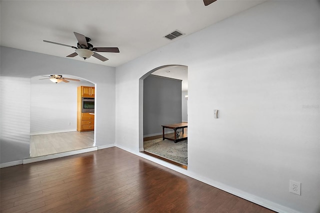 empty room featuring arched walkways, dark wood finished floors, visible vents, ceiling fan, and baseboards