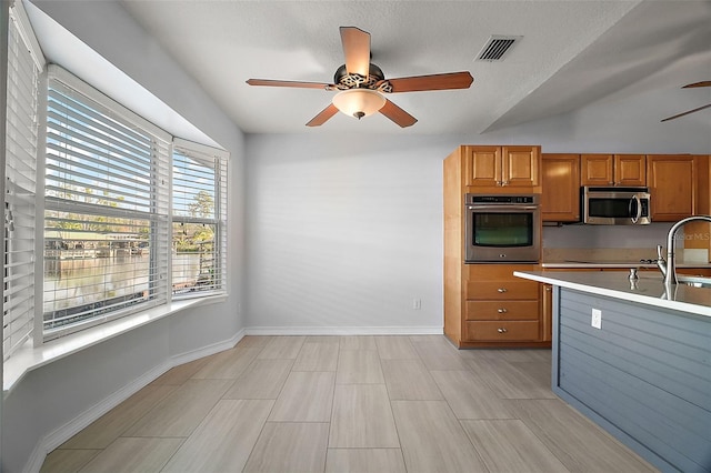 kitchen featuring brown cabinets, stainless steel appliances, light countertops, visible vents, and ceiling fan