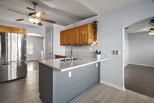 kitchen featuring wood finish floors, arched walkways, freestanding refrigerator, a sink, and a peninsula