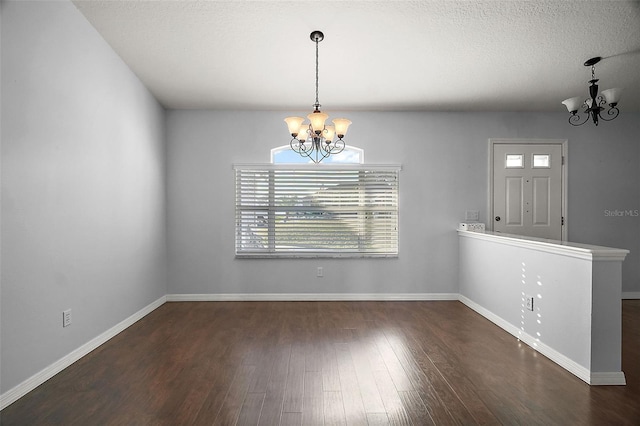 unfurnished dining area with a chandelier, a textured ceiling, baseboards, and wood finished floors