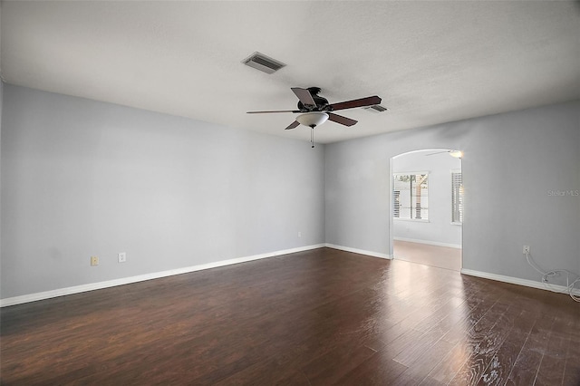 empty room with arched walkways, wood finished floors, visible vents, and a ceiling fan