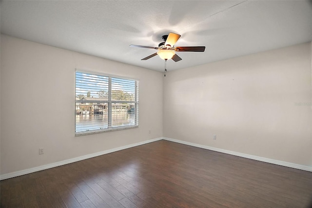 spare room featuring dark wood-type flooring, a ceiling fan, and baseboards