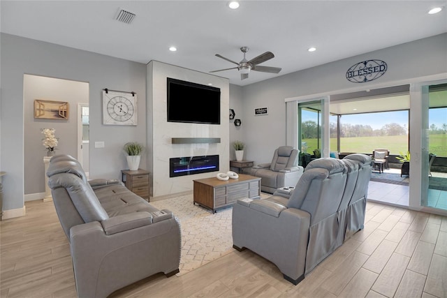 living room with ceiling fan, a large fireplace, and light hardwood / wood-style flooring