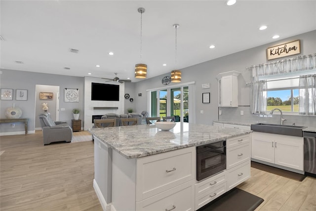 kitchen featuring sink, a center island, black microwave, a large fireplace, and white cabinets