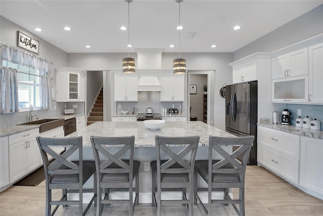 kitchen with hanging light fixtures, black fridge, sink, and a large island