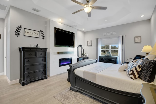 bedroom with ceiling fan, light wood-type flooring, and a tray ceiling