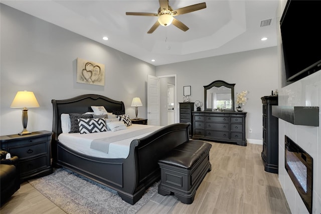 bedroom with light hardwood / wood-style floors, a raised ceiling, and ceiling fan