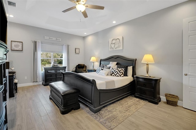 bedroom featuring a raised ceiling, ceiling fan, and light wood-type flooring