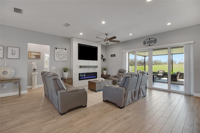 living room featuring ceiling fan, a fireplace, and light hardwood / wood-style floors