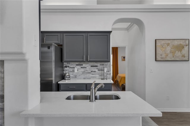 kitchen with gray cabinetry, stainless steel refrigerator, light stone countertops, sink, and tasteful backsplash