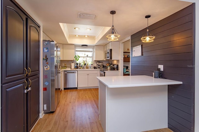 kitchen with visible vents, a tray ceiling, a peninsula, a sink, and stainless steel appliances