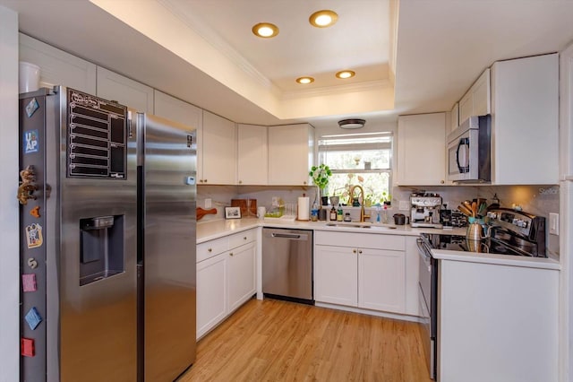 kitchen featuring a sink, stainless steel appliances, light wood-style floors, white cabinets, and a raised ceiling