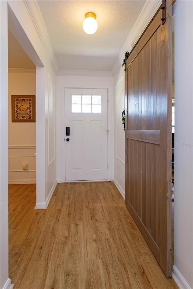 entryway with crown molding, light wood-style floors, a textured ceiling, a barn door, and a decorative wall