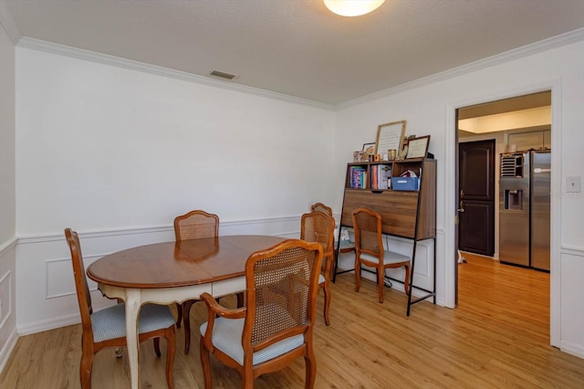 dining room featuring ornamental molding, light wood-type flooring, visible vents, and wainscoting