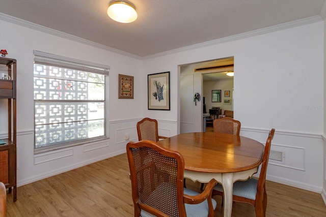 dining area with light wood-style floors, crown molding, and a decorative wall