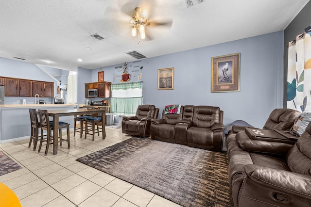 living room featuring ceiling fan, light tile patterned floors, sink, and a textured ceiling