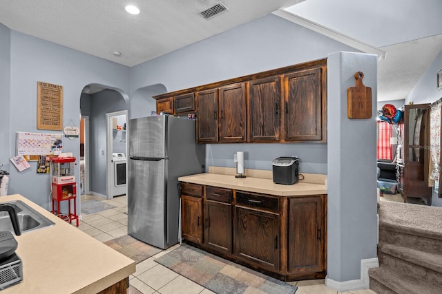 kitchen featuring stainless steel refrigerator, sink, dark brown cabinets, light tile patterned floors, and a textured ceiling